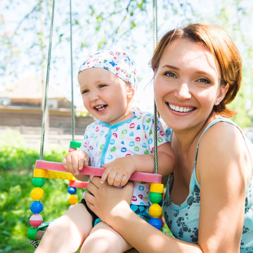 Happy Mother With Laughing Baby Sits On Swing