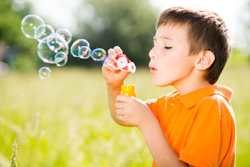Young caucasian boy blowing the soap bubbles on nature
