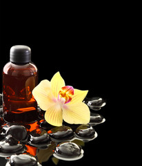 Black Zen stones and essential oil bottle on calm water