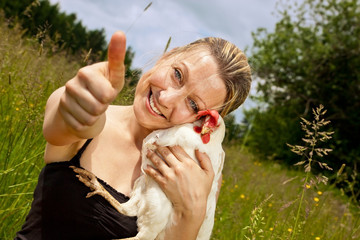 Frau mit Huhn im Arm hält Daumen hoch