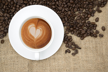 Cup of coffee with heart shape in foam on hessian background