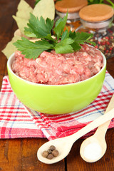 Bowl of raw ground meat with spices on wooden table