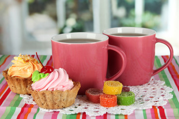 Cups of tea with cake and candy on table in room