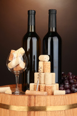 Naklejka premium Wine and corks on barrel on brown background