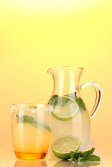 Lemonade in pitcher and glass on yellow background