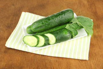Tasty green cucumbers on color napkin, on wooden background