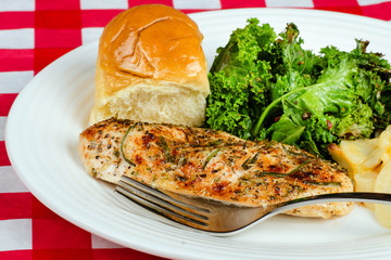 Herb-crusted baked chicken breast with kale and buttered roll