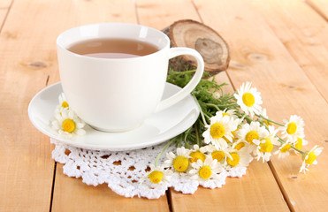 Fototapeta na wymiar Cup of chamomile tea and chamomile on wooden table