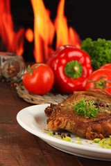 Piece of fried meat on plate on wooden table on fire background