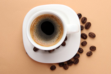 Cup of coffee with coffee beans on beige background