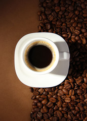 Cup of coffee with coffee beans on brown background