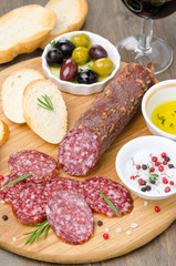 Italian salami, bread, olives and spices on a cutting board