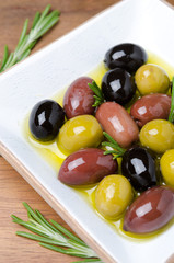 white wooden bowl with variety of olives and rosemary in oil
