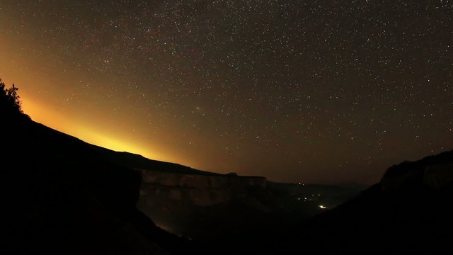 Time lapse of the night sky with clouds and stars passing by beh