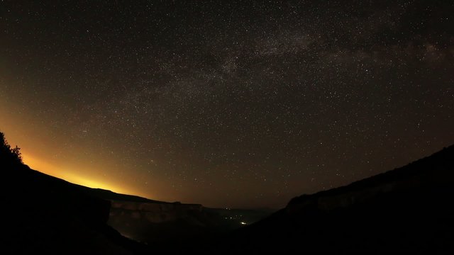 Time lapse of the night sky with clouds and stars passing by beh