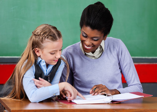 Teacher Assisting Schoolgirl At Desk