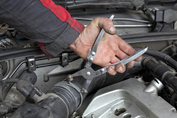 Mechanic fix hose clamp with pliers tool at car engine