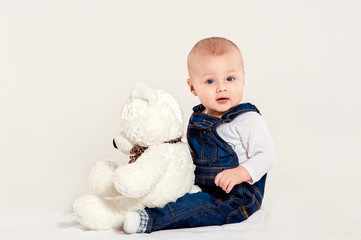 the little boy in blue overalls plays with a teddy bear