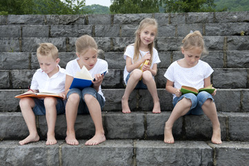 summer holidays: children with a book seated outdoors on stairs