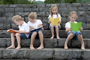 summer holidays: children with a book seated outdoors on stairs