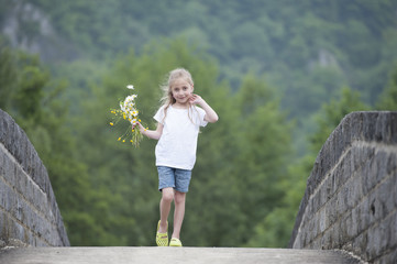 little girl with a bouquet of daisies walking outdoors © aldegonde le compte