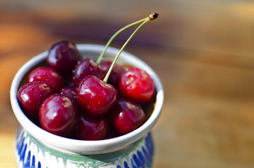 Ripe cherries in a rustic recipient on a wooden surface.