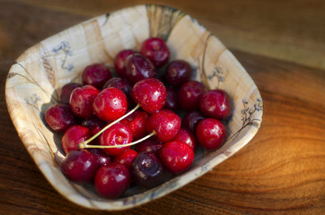 Ripe cherries in a rustic recipient on a wooden surface.