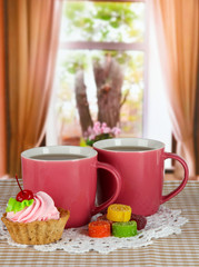 Cups of tea with cake and candy on table in room