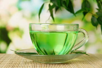 Transparent cup of green tea on bamboo mat, on nature
