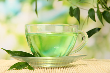 Transparent cup of green tea on bamboo mat, on nature