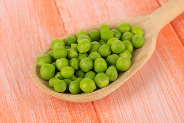 Sweet green peas in spoon on wooden background