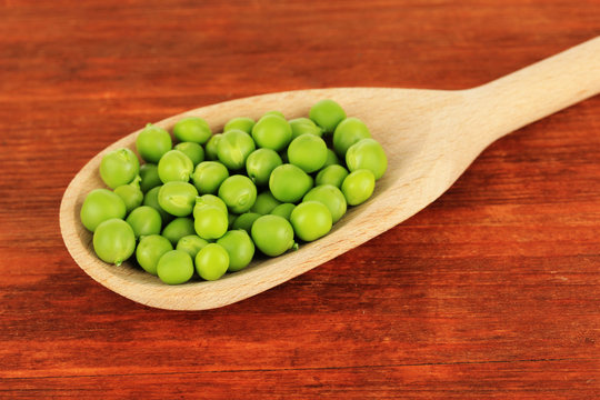 Sweet green peas in spoon on wooden background