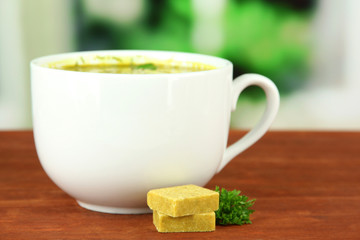 Cup of soup with bouillon cubes on wooden table