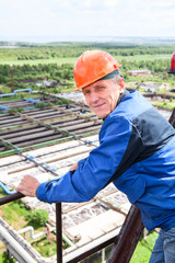 Senior engineer worker in blue uniform and hardhat on altitude