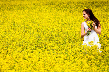 Beautiful Woman in white dress holding a bunch of rape flowers. - 53680027