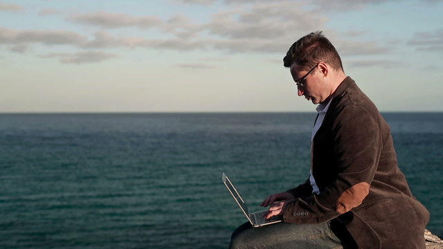 Young man sitting on rocks near the vantage point with laptop co