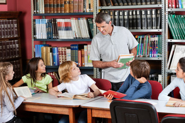 Teacher Communicating With Students Sitting At Table In Library