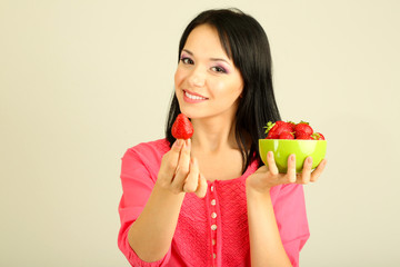 Beautiful young woman with strawberries on grey background