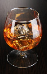 Brandy glass with ice on wooden background