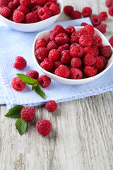 Ripe sweet raspberries in bowls on wooden background