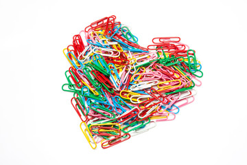 Multi color paper clips arranged in heart shape on isolated white background
