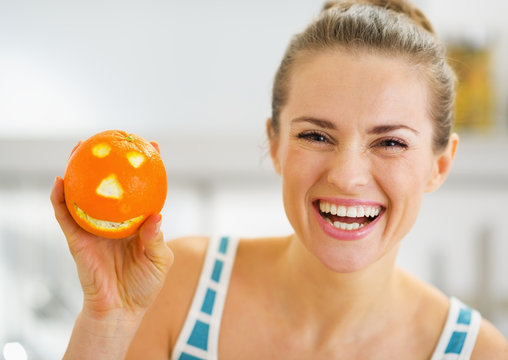 Smiling young woman showing orange with funny face