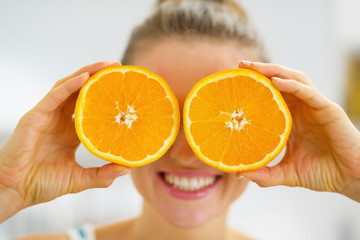 Happy young woman holding two slices of orange in front of eyes