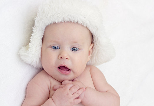 Surprised cute blue eyed baby in fur hat with crossed hands
