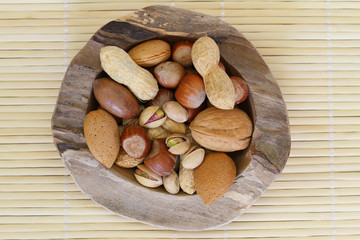Mixed nuts in teak root bowl on bamboo mat