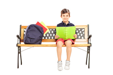 Schoolboy sitting on a wooden bench and reading a book