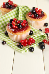 Tasty muffins with berries on white wooden table