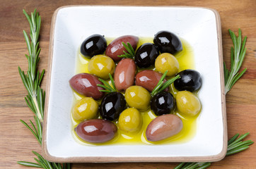 white wooden bowl with a variety of olives and rosemary in oil