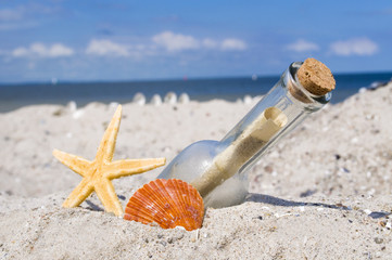 Flaschenpost im Sand mit Muschel und Seestern