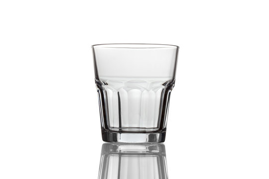 Empty glass for whiskey on a reflective surface on white backgro
